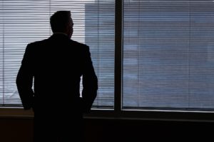 Business man looking out the window of an office thinking about whether his actions constituted white collar crimes